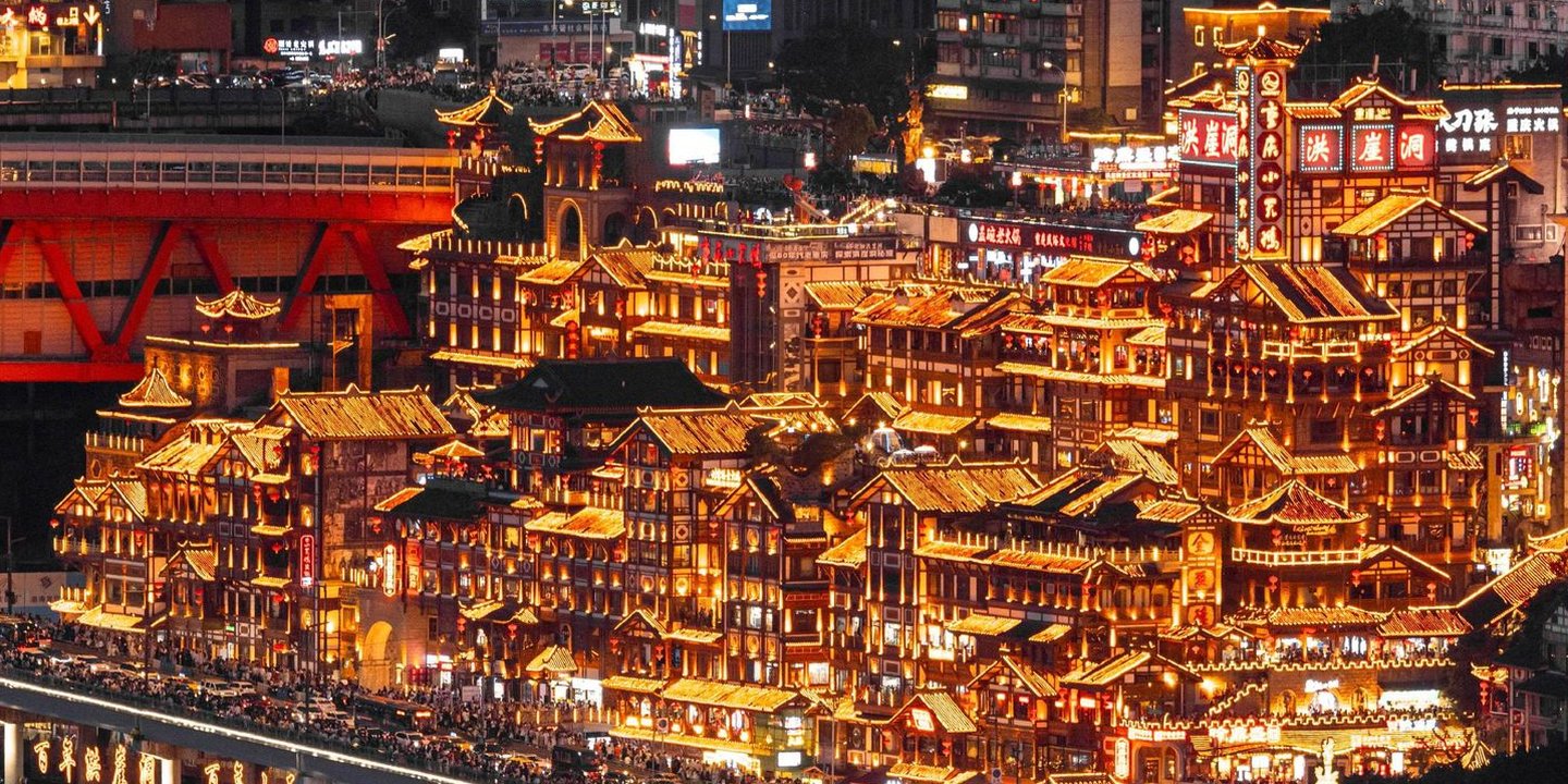 Hongya Cave stilt houses fully illuminated at night with cruise boats on the river